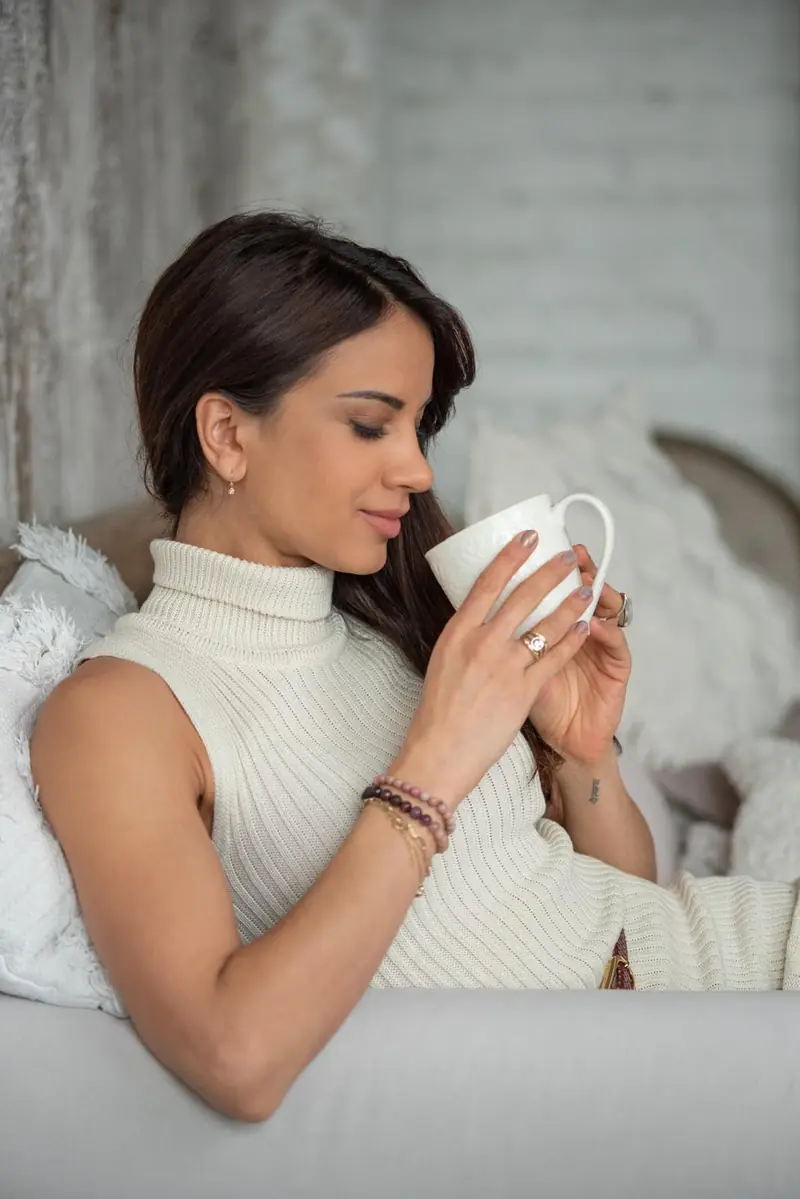 Eniko resting on a sofa with her eyes closed, holding a warm cup with both hands